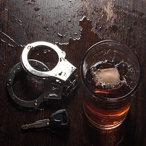 Handcuffs, car key, and whiskey glass on wood, symbolizing a DWI arrest or legal defense